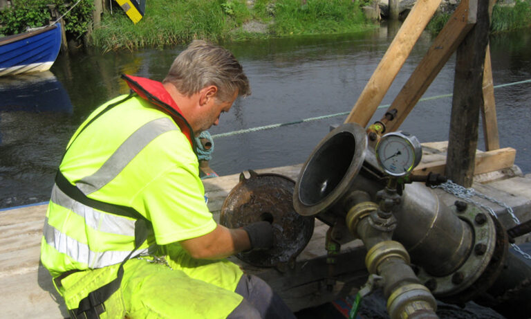 En anställd från Pollex jobbar med ett rör som går ned i vattnet